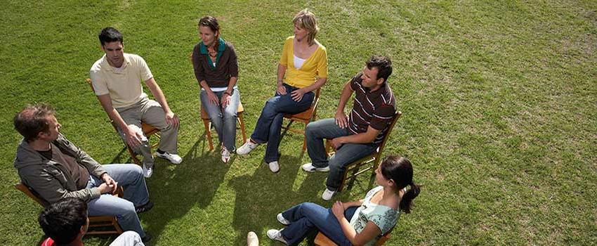 A group of people sitting in chairs in a circle outside talking.