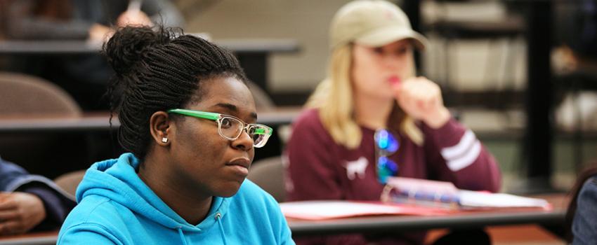 Female student with glasses sitting in classroom listening to lecture,