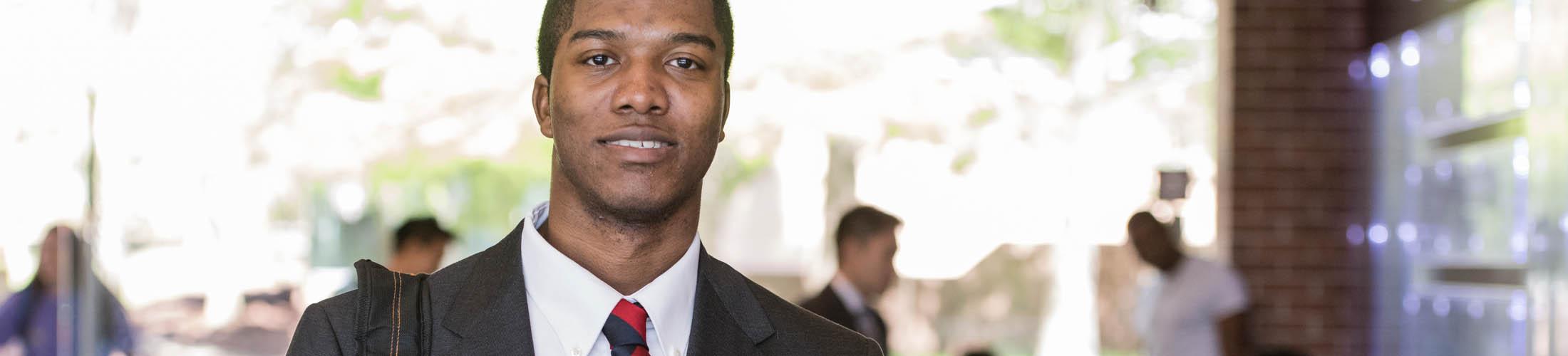 Male student dressed in a suit walking outside on campus.