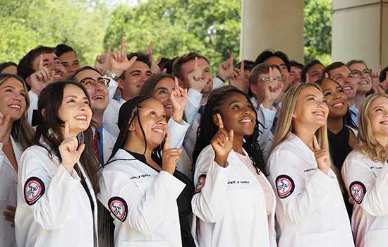 College of Medicine students in white coats holding up J hand.